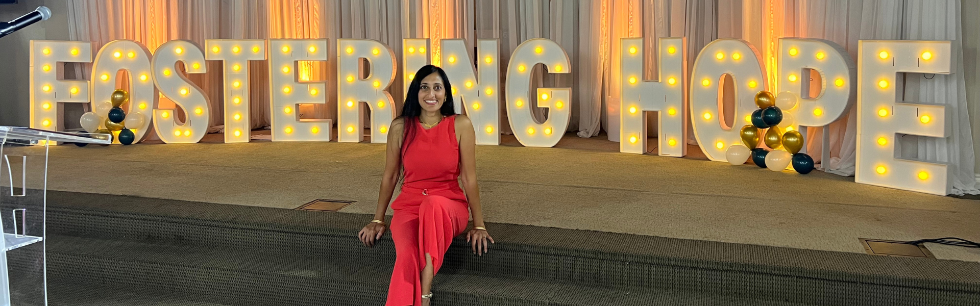 Manisha in front of a lit sign that says 