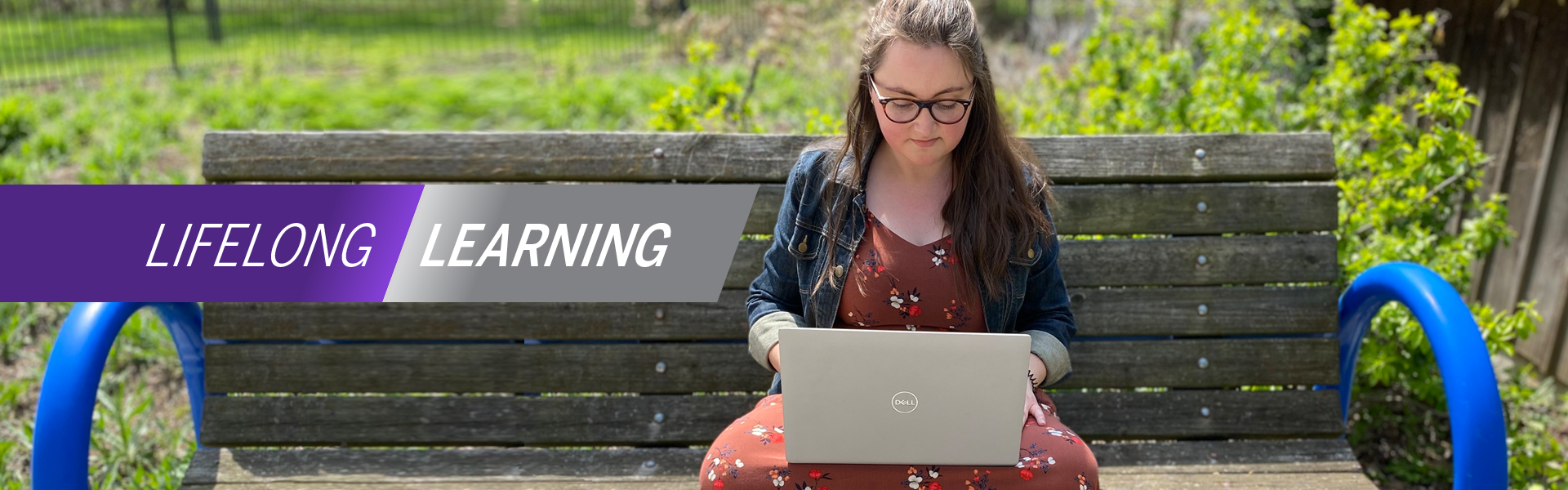 Young alum studies at a laptop while seated on an outdoor bench