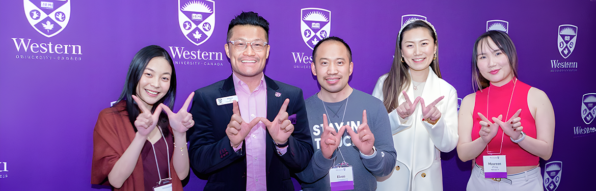 Group of alumni in front of a purple Western background
