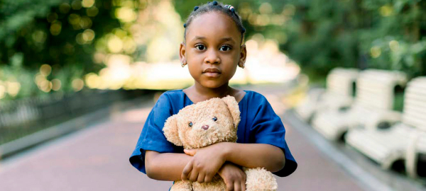 A young girl stares to the camera as she holds a teddy bear.