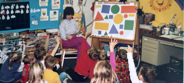 In this vintage photo, a teacher is seen instructing a class of young children.