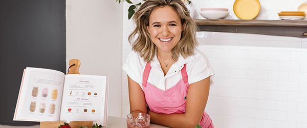 Carleigh Bodrug leaning on a counter with a open cookbook and fruit