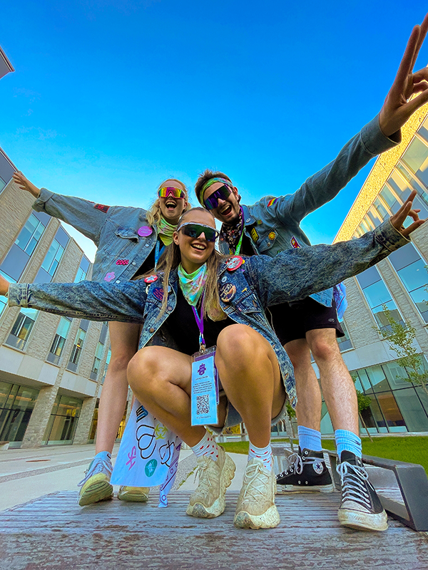 Three FIMS Sophs dressed in jean jackets and sunglasses on a sunny day outside of FIMS & Nursing Building on campus.