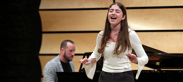 Young singer performing on stage in von Kuster Hall with piano behind her