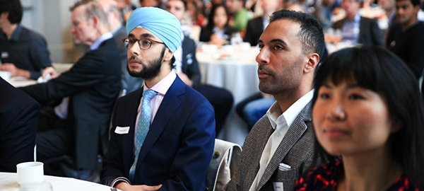 Three people in business attire sit at a table listening to a presentation 