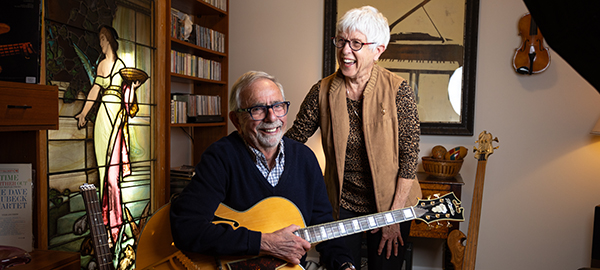 Jim and Barbara Moscovich, Jim holds a guitar and Barbara is laughing