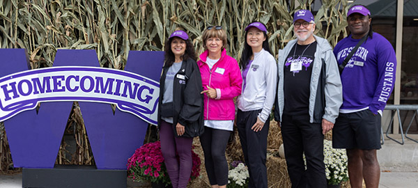 A group poses together in front of a Homcomingsign