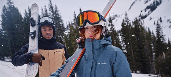 Two people with skies wearing skiing gear on a mountain