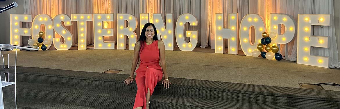Manisha in front of a lit sign that says