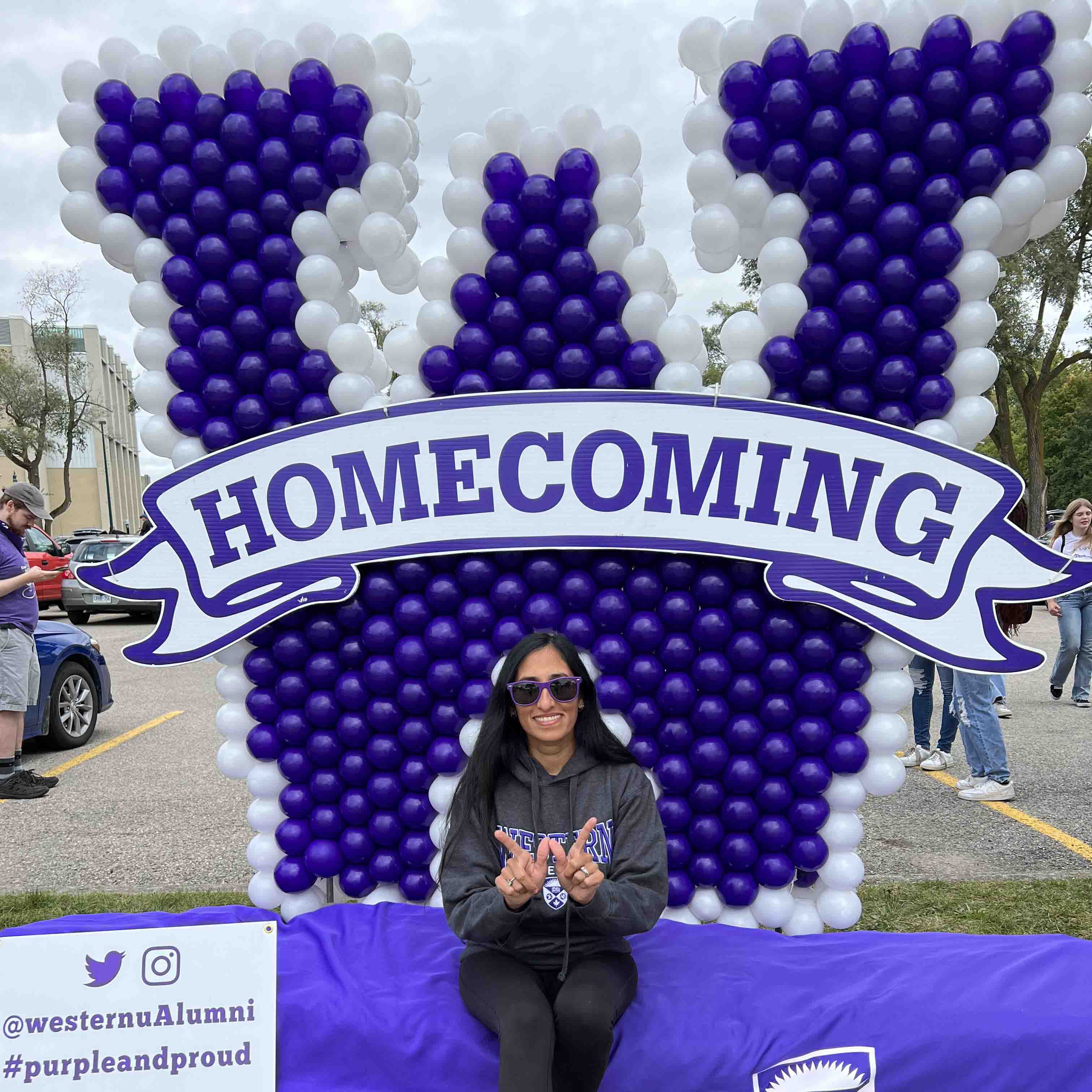 Manisha homecoming Manisha sits in front of a large W made of purple and white balloons, a sign on the W says